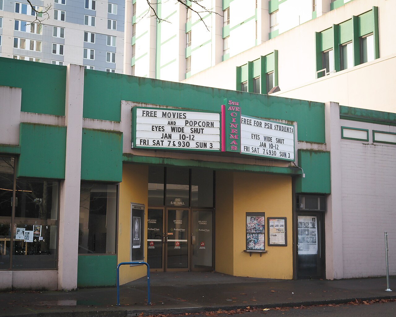 5th Avenue Cinema's green-and-yellow storefront, vertical sign, and marquee reading 'Free Movies and Popcorn' on SW Hall Street