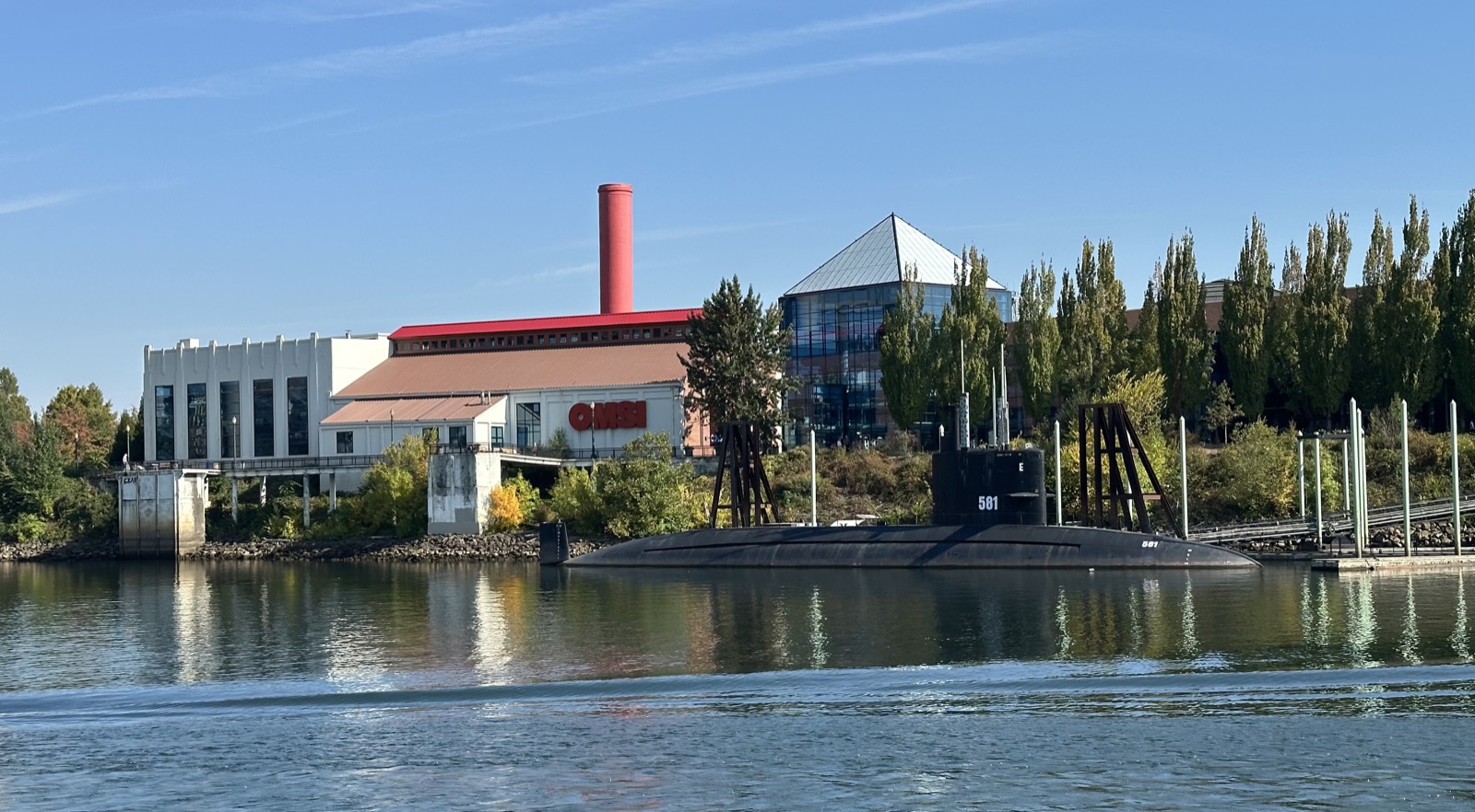 OMSI's riverfront campus on the Willamette — its red smokestack, glass atrium, and the USS Blueback submarine moored in front